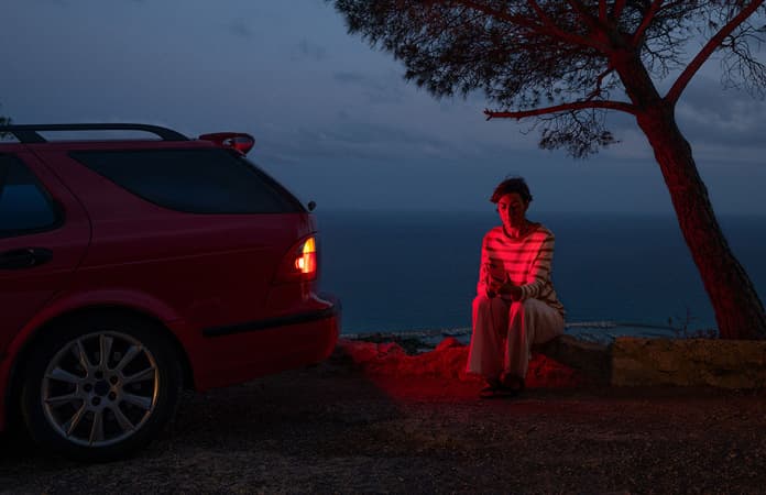 A photo of a car stranded by the side of a road, one person by the car using Roadside Assistance via satellite on iPhone